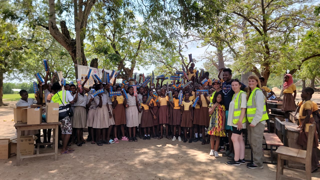 Schoolgirls holding up their new dignity kits with volunteers