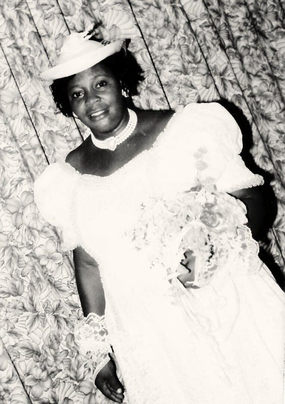 A black-and-white photo of a young Josephine in a white dress and hat, holding flowers