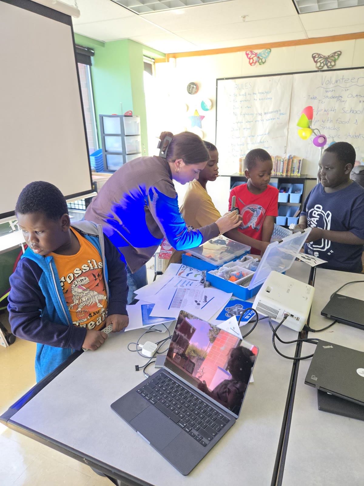 A volunteer helps students at their laptops in a Utah robotics class